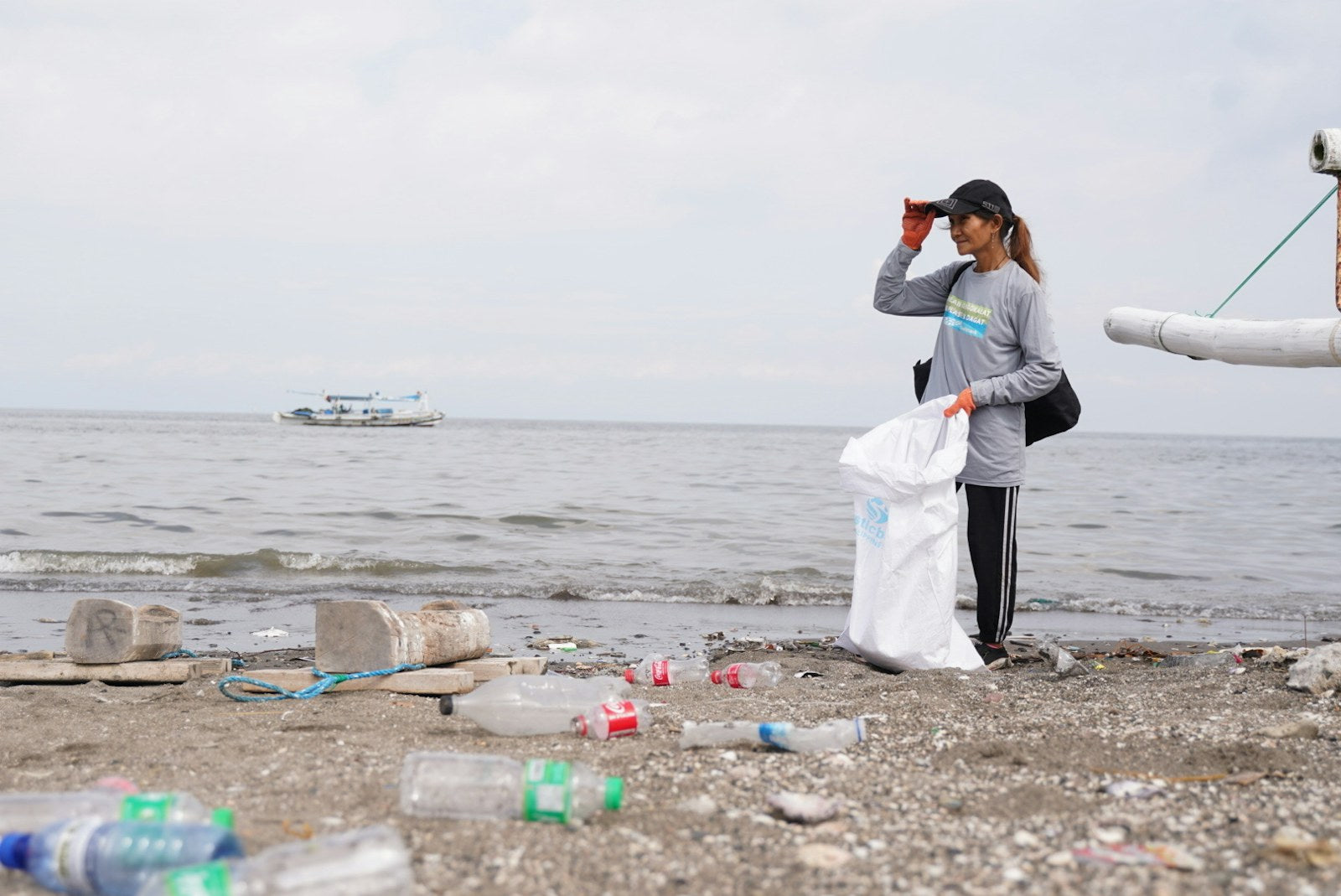 A coastal cleanup worker collecting plastic from a shoreline in the Philippines